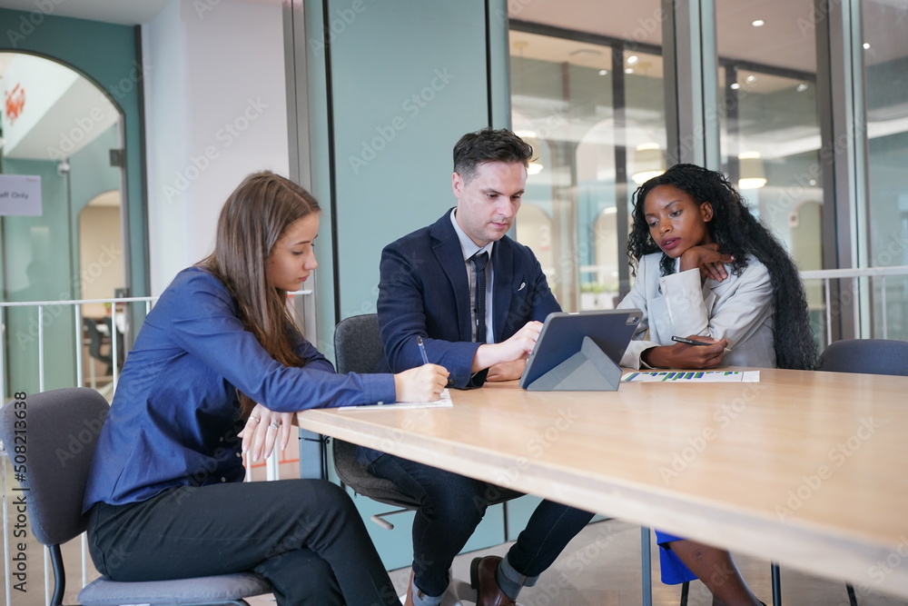 Image of young businessmen and colleague discussing document in laptop and touchpad at meeting Image of young businessmen and colleague discussing document in laptop and touchpad at meeting