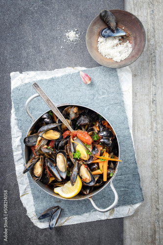 Traditional Italian sailors mussel in white wine sauce with vegetables served as top view in a rustic casserole
