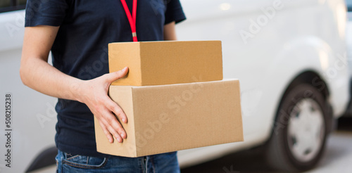 Detalle de medio cuerpo y cajas de cartón de repartidor, en la entrega del pedido. Fotografía horizontal con espacio para texto.