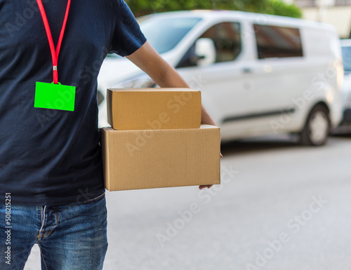 Repartidor irreconocible, con dos cajas de cartón para entregar a casa, con tarjeta de bienvenida con croma verde. Fotografía horizontal con espacio para texto.