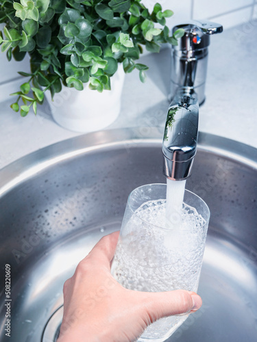 A stream of clean water drink flows into the glass. Woman holding a glass of water under running water from the tap in the kitchen.
