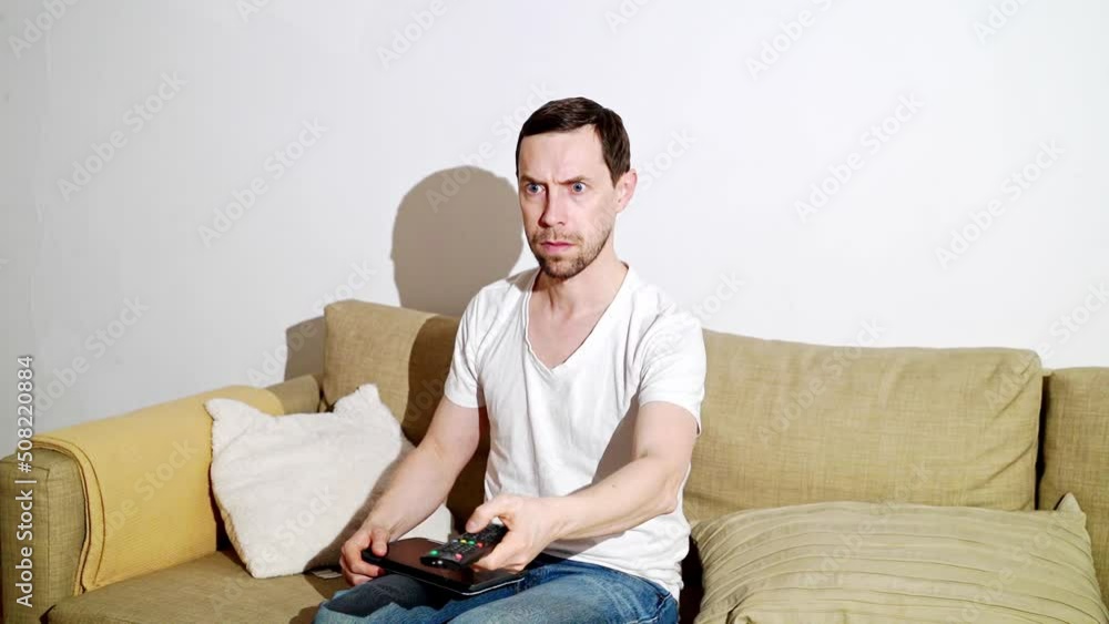 Young man switch at living room. Home vacation sofa portrait. Watch tv video. Alone in interior. Happy emotion. Smiling male person. Lifestyle action. House light background Young man switch at living room. Home vacation sofa portrait. Watch tv video. Alone in interior. Happy emotion. Smiling male person. Lifestyle action. House light background