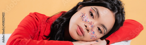 Stylish asian model with glitter makeup sitting in bathtub isolated on orange, banner.