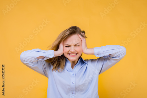 Headache. Emotional girl embraces her head with her hands in pain on a yellow background. Migraine.