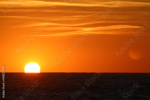 Sun on horizon. Tranquil scenery of sunset on sea. Calm sea water  cloudy orange sky. Beautiful evening on the beach. 