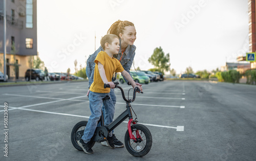 Mom helps a child boy learn to ride a two-wheeled bicycle in the park. A pleasant children's summer sports vacation