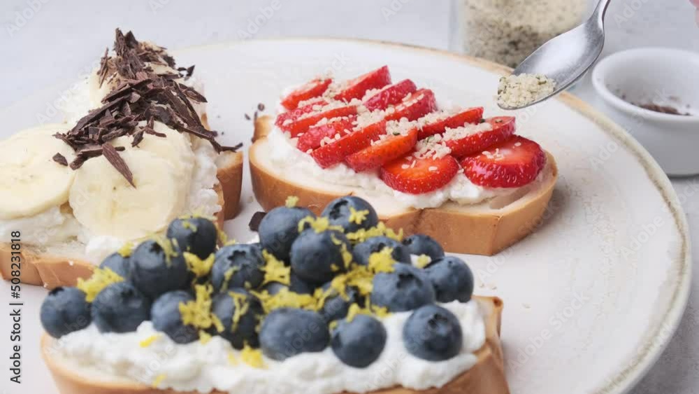 Cooking fruit vegetarian toasts for breakfast. Bread slices with ricotta, berries, banana, chocolate and seeds. Cooking fruit vegetarian toasts for breakfast. Bread slices with ricotta, berries, banana, chocolate and seeds.