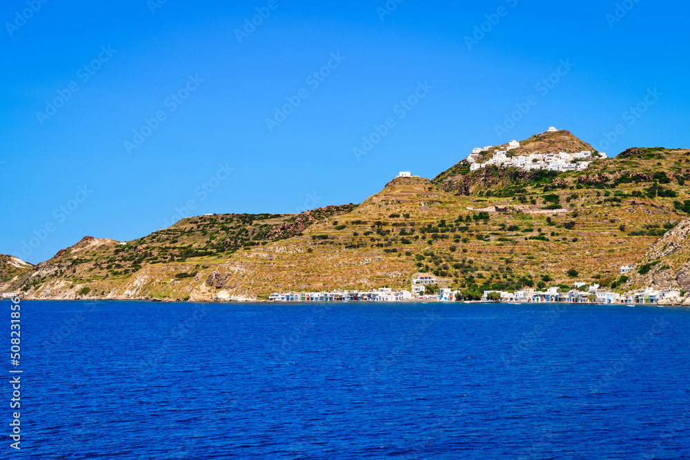 Beautiful summer day of Greek island town oh hill top by seafront. Whitewashed houses by waterfront. Mediterranean vacations. Milos, Cyclades, Greece.