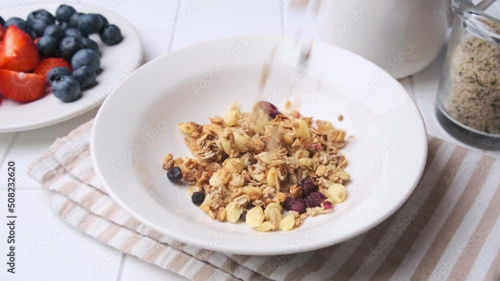 Slow motion pouring granola into a white plate. Cooking breakfast concept. Slow motion pouring granola into a white plate. Cooking breakfast concept.
