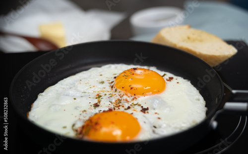 Close up of fried eggs with spices and seasonings in hot frying pan. Breakfast