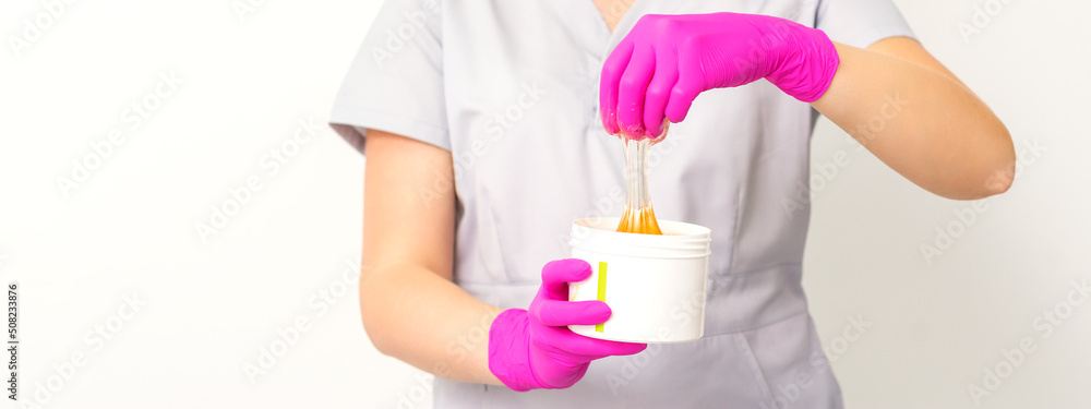 Portrait of a female caucasian beautician holding a jar of sugar paste for sugaring wearing pink gloves on white background Portrait of a female caucasian beautician holding a jar of sugar paste for sugaring wearing pink gloves on white background