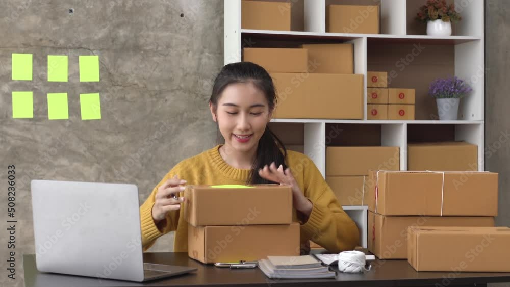 Young asian woman writing address on parcel box at home for delivery order to customer. Young asian woman writing address on parcel box at home for delivery order to customer.