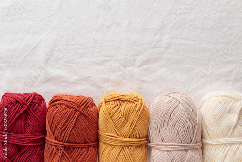 Fotografia, Obraz Balls of cotton yarn warm colors on a white textile table, top view close up ban