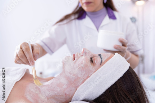 Cosmetologist applying a face mask to a client's face in a beauty salon, spa