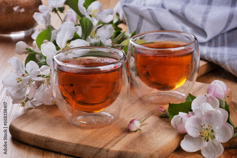 two glass cups with tea and apple tree flowers on a wooden table. rural still life two glass cups with tea and apple tree flowers on a wooden table. rural still life