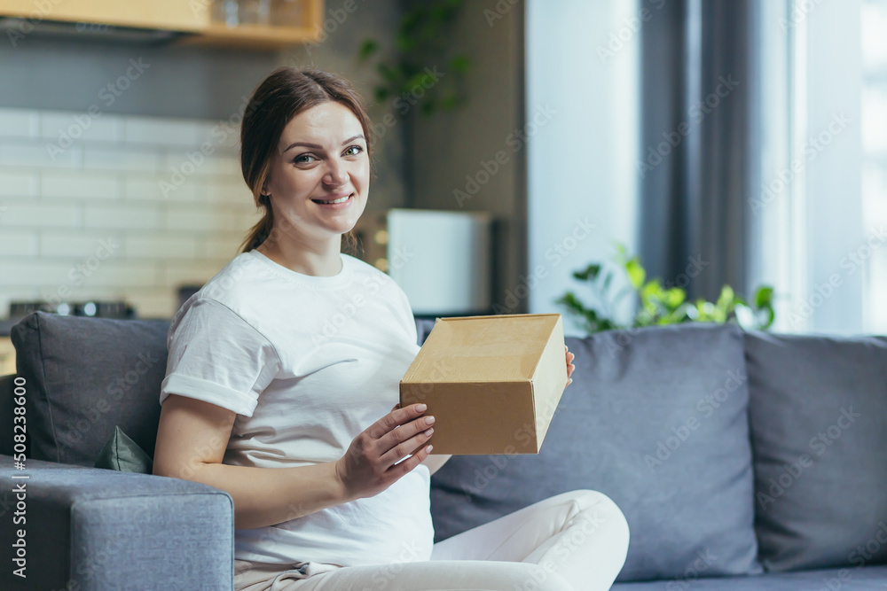 Pregnant beautiful woman received a parcel by courier home, package, gift. He sits on the sofa at home, opens a paper box, rejoices, smiles Pregnant beautiful woman received a parcel by courier home, package, gift. He sits on the sofa at home, opens a paper box, rejoices, smiles