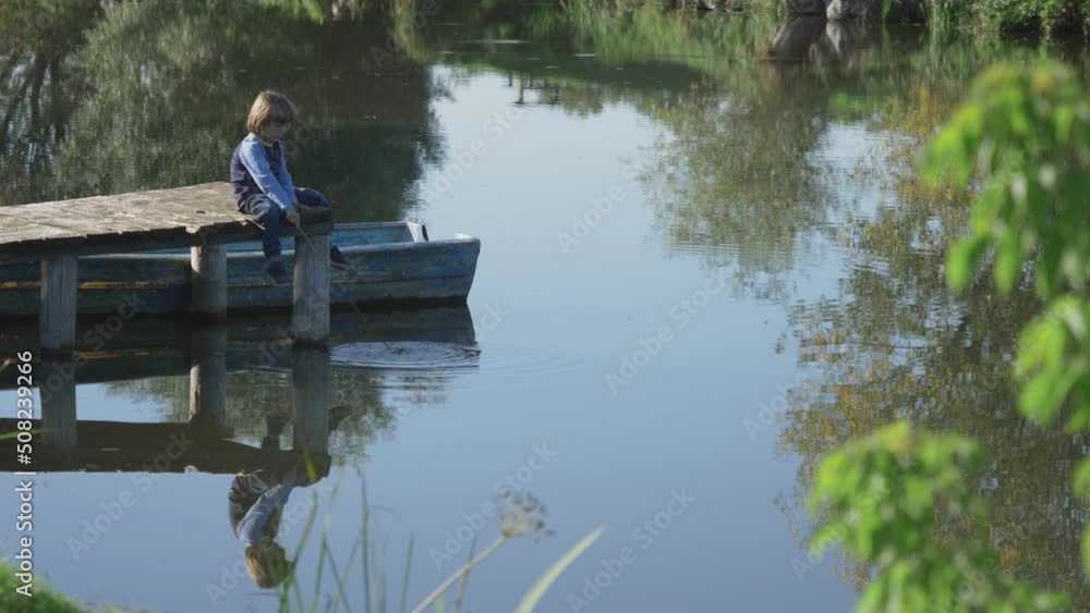Little kid playing with a stick in the water, playing the fisherman with rod on wooden pontoon Little kid playing with a stick in the water, playing the fisherman with rod on wooden pontoon