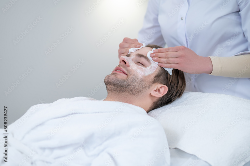 Cosmetologist removing the facial mask from the clients face Cosmetologist removing the facial mask from the clients face