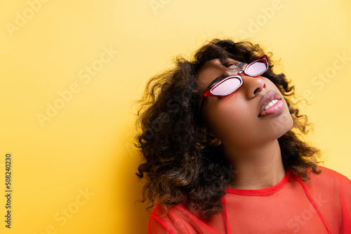 brunette african american woman in fashionable sunglasses on yellow background. © LIGHTFIELD STUDIOS