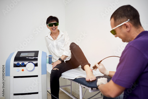 Feet laser therapy. Physiotherapist doctor uses Laser medical equipment for highly effective feet pain treat. Concept of medical orthopedic treatment and rehabilitation photo