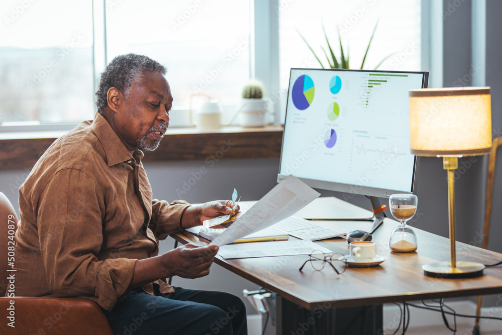 Shot of a senior man looking stressed while going through paperwork at home. Man analyzes month expenses feels concerned about public utility debt Shot of a senior man looking stressed while going through paperwork at home. Man analyzes month expenses feels concerned about public utility debt