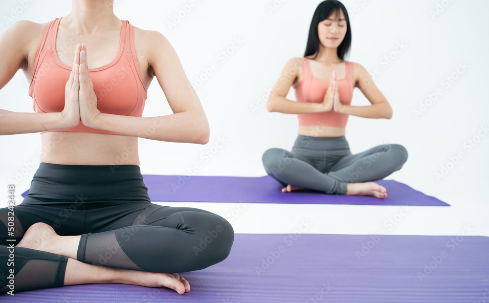 Wellness Couple Asian young woman sit meditation yoga mat doing breathing exercise yoga lotus pose together.Yoga meditation of two healthy female relax and comfortable at cozy home.Healthy lifestyle.