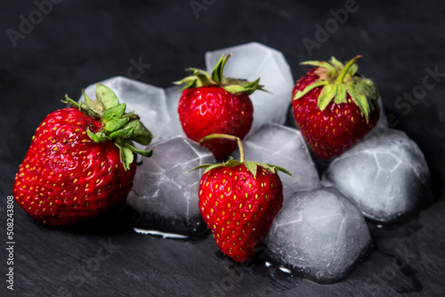 Strawberries with ice on a black background. cold refreshing fruit