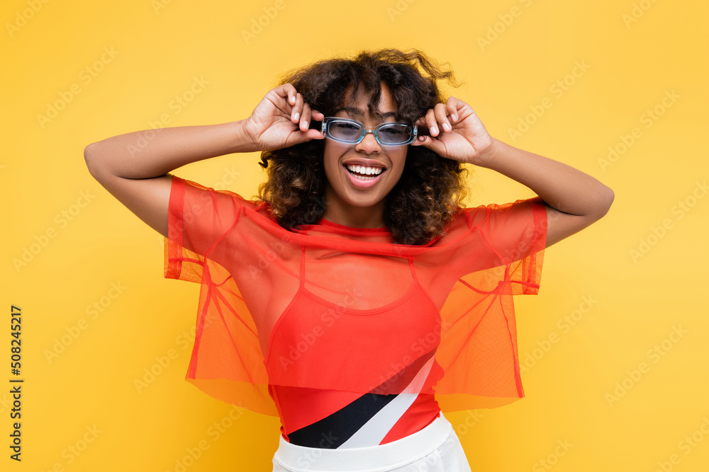 happy african american woman in trendy summer clothes adjusting sunglasses isolated on yellow. happy african american woman in trendy summer clothes adjusting sunglasses isolated on yellow.