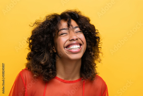 overjoyed african american woman smiling with closed eyes isolated on yellow. photo