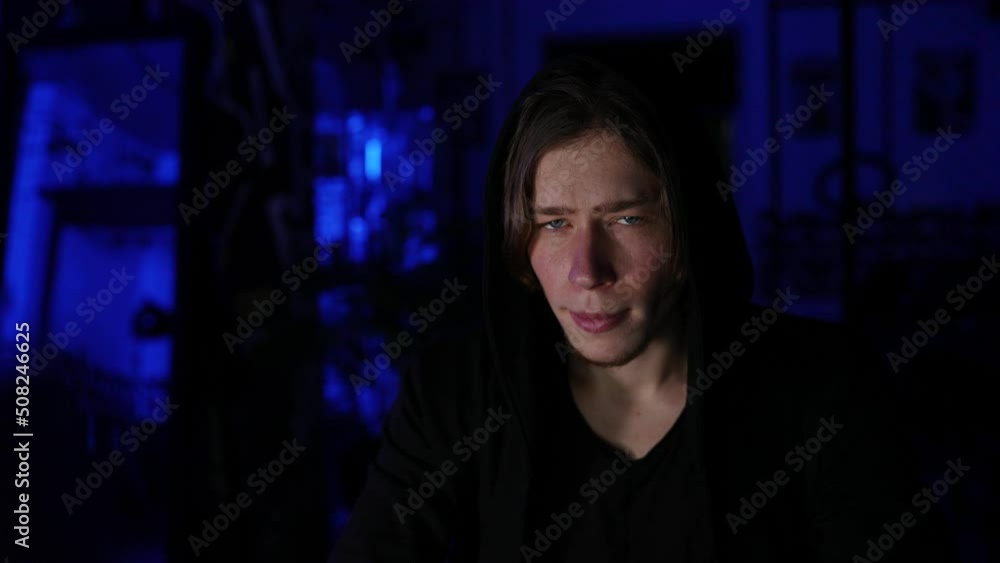 Close-up tracking shot of face of focused hacker man in black sweatshirt using laptop and desktop computer to breaking network system, from dark room with blue neon lights. Shooting in slow motion. Close-up tracking shot of face of focused hacker man in black sweatshirt using laptop and desktop computer to breaking network system, from dark room with blue neon lights. Shooting in slow motion.