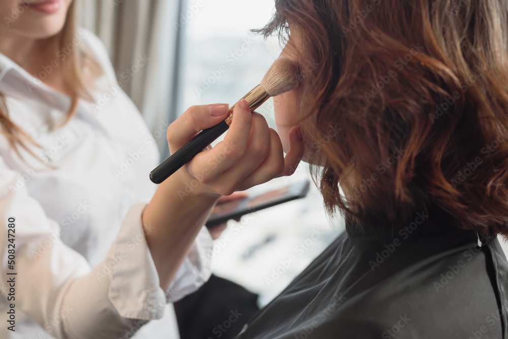 Professional female artist applying cosmetic powder on client's face for perfect skin Professional female artist applying cosmetic powder on client's face for perfect skin