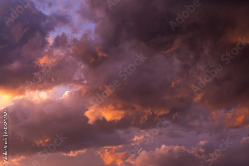 Epic sunset storm sky. Big grey violet cumulus thunderstorm clouds in orange sunlight background texture 