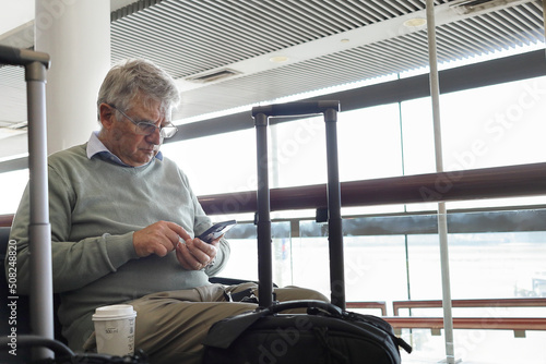 Older man sitting at the airport checking his cell phone