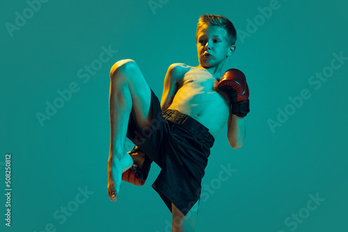 Young sportsmen, beginner fighter of mma sport in action isolated on cyan color background. Sport, education, action, motion concept. photo