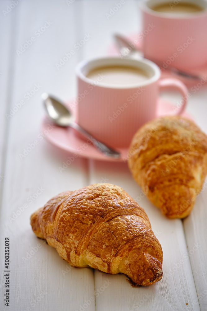 A crispy croissant with almond filling and Coffee with cream on a white wooden table. A crispy croissant with almond filling and Coffee with cream on a white wooden table.