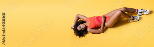 top view of brunette african american woman in beachwear lying on yellow background, banner.
