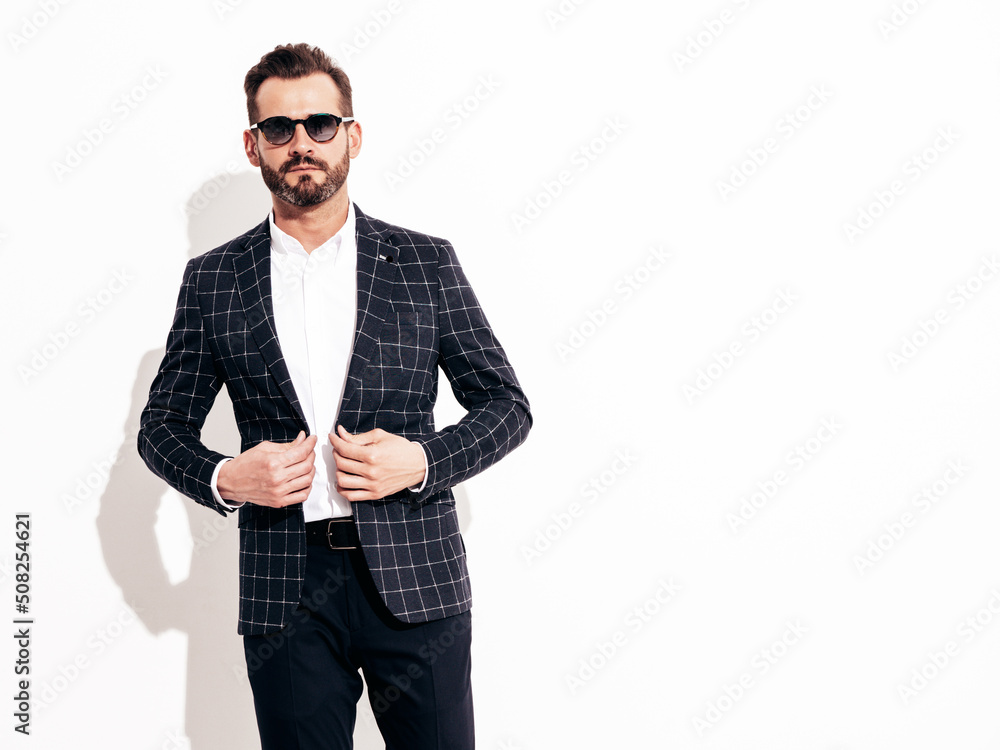 Fototapeta premium Portrait of handsome confident stylish hipster lambersexual model. Sexy modern man dressed in black elegant suit. Fashion male posing in studio in sunglasses. Isolated