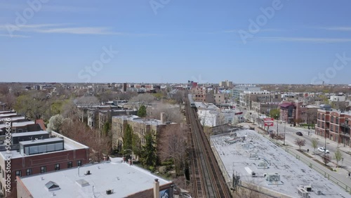 Gray subway rides at high speed on an elevated subway track as the subway is reflected in a building in a new suburb of Chicago on a sunny day. Fast drone dolly shot photo