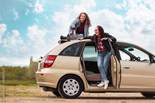 Happy mother and her teen daughter funny posing by a car. The concept of freedom and travel on a car