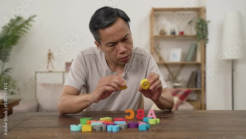 asian senior male Alzheimer’s patient practicing rehab treatment with color letter bricks at home. he compares two blocks and puts them in order on table