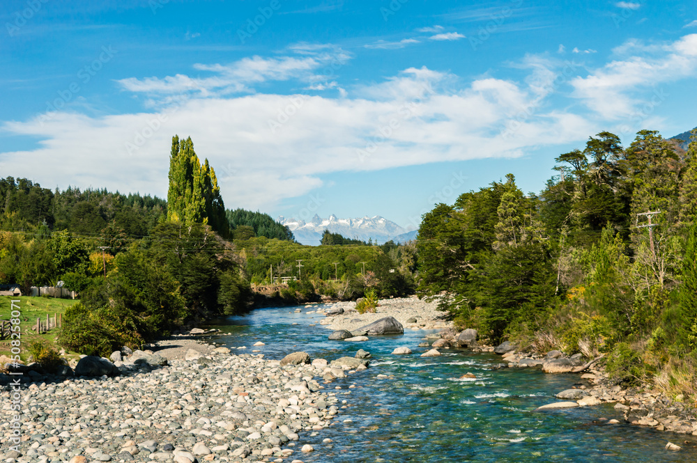 Translucent river with forest on its coast and a snowy mountain range in the background