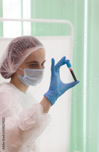a masked nurse shakes a test tube with blood to conduct a qualitative analysis of the patient's blood