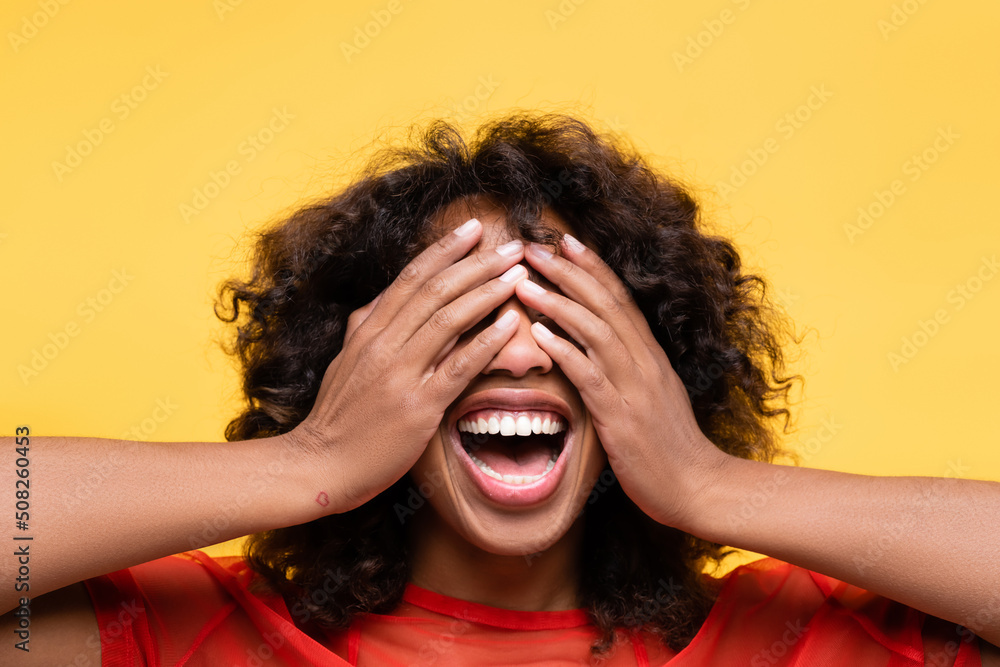 astonished african american woman covering eyes with hands isolated on yellow. astonished african american woman covering eyes with hands isolated on yellow.
