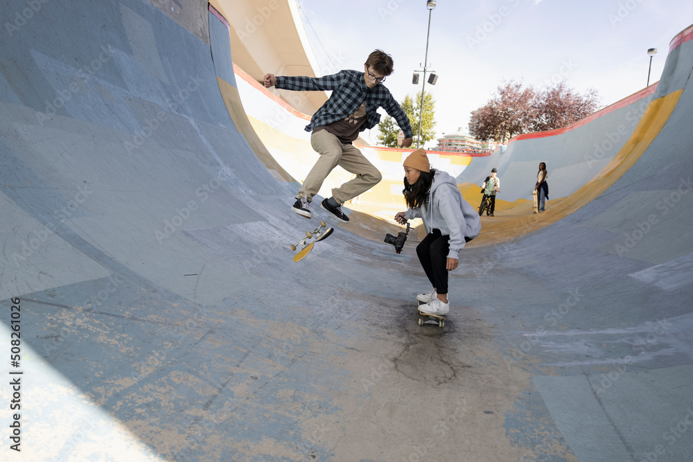 Asian teen girl filming friend doing trick on skateboard in tunnel Photos |  Adobe Stock