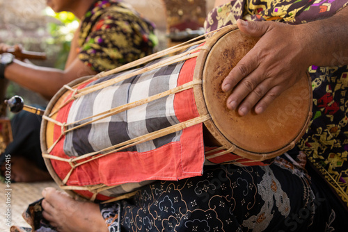 A musician plays a kendhang or ketipung, a traditional Balinese instrument, as part of a musical ensemble or gamelan, during a performance photo