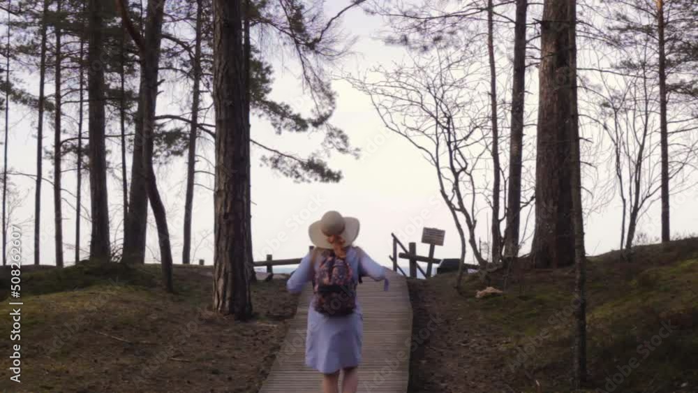 Woman walking through boardwalk walkway of wood towards sea coastline Woman walking through boardwalk walkway of wood towards sea coastline