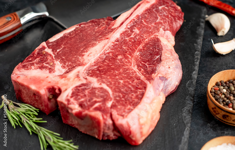 Raw Porterhouse or T-bone beef meat Steak with herbs on stone background