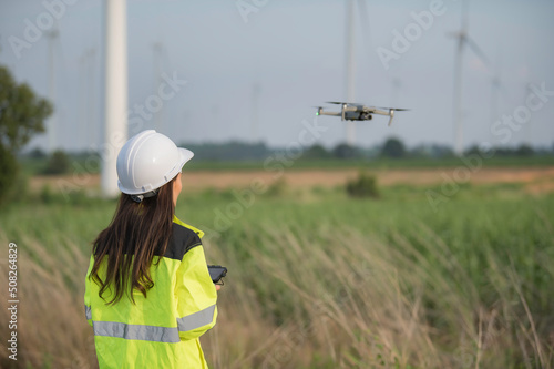 Engineers working and holding the report at wind turbine farm Power Generator Station on mountain,Thailand people,Technician man and woman discuss about work.,Use drone view from high angle