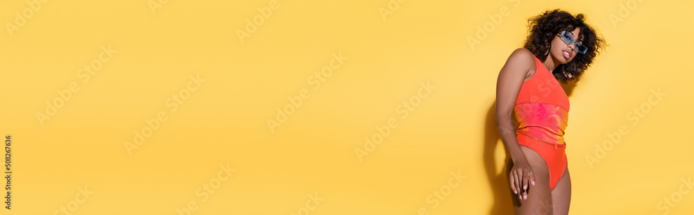 curly african american woman in trendy sunglasses and swimsuit on yellow background, banner. curly african american woman in trendy sunglasses and swimsuit on yellow background, banner.