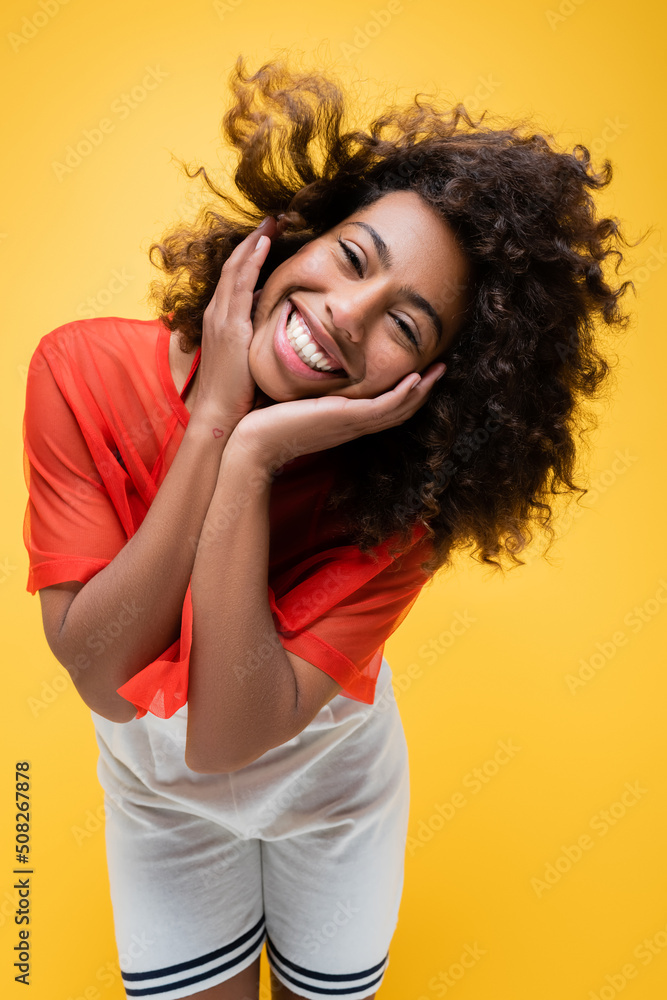 cheerful african american woman in summer clothes touching face isolated on yellow. cheerful african american woman in summer clothes touching face isolated on yellow.